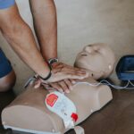 Hands demonstrating CPR technique on a training mannequin with AED.